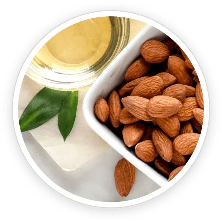 Sweet almond oil in a glass bottle with fresh almonds scattered around, representing natural nail nourishment.